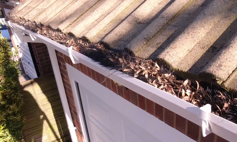 A sloped roof with a white gutter filled with dry leaves and debris