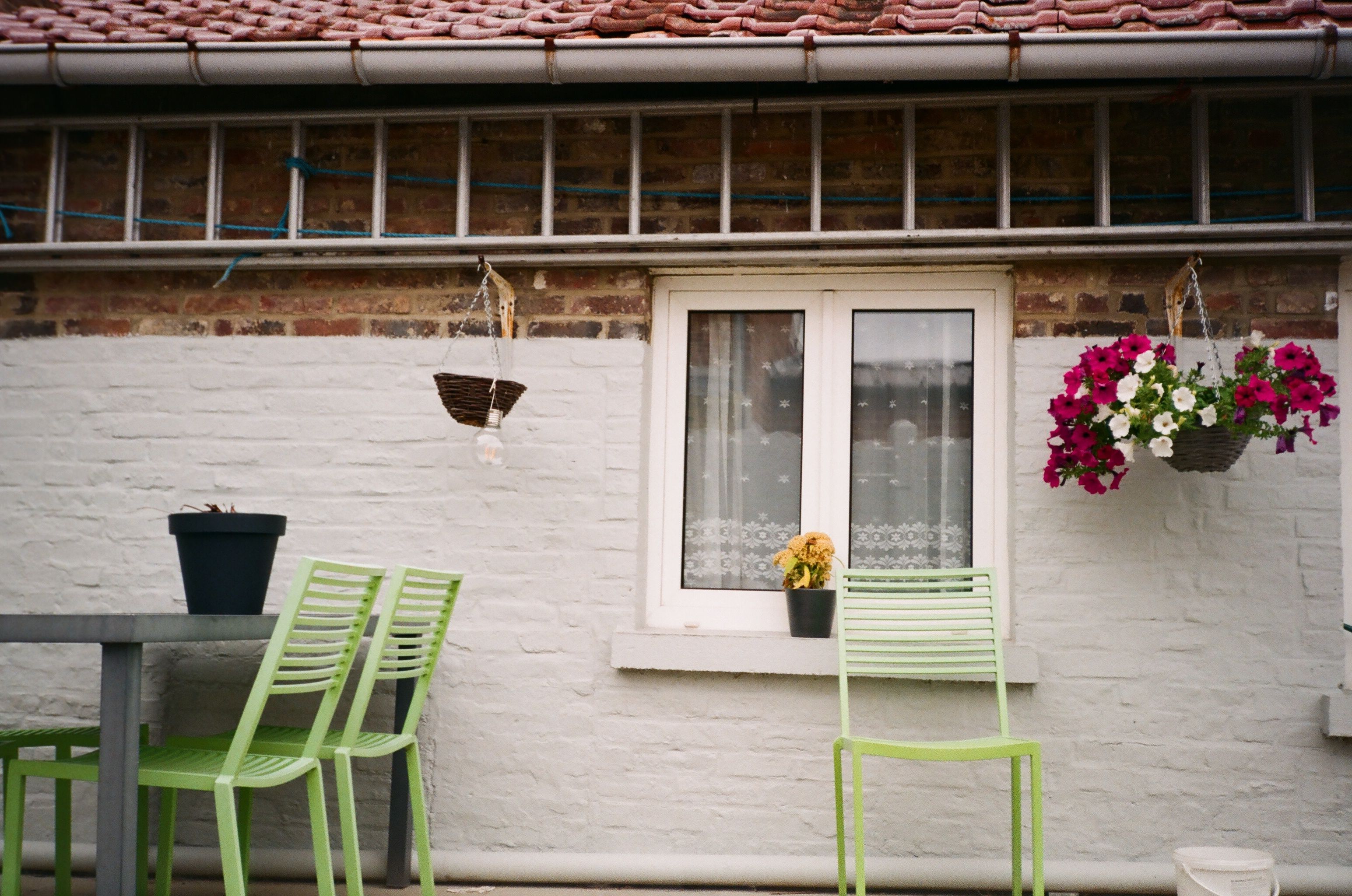 Compact patio with green chairs, hanging flowers, and a brick wall, offering inspiration for a colorful garden makeover.